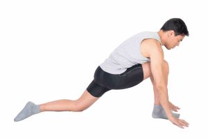 Deportista realizando un estiramiento del músculo psoas en un gimnasio, destacando la importancia de la técnica y la concentración para la prevención de lesiones