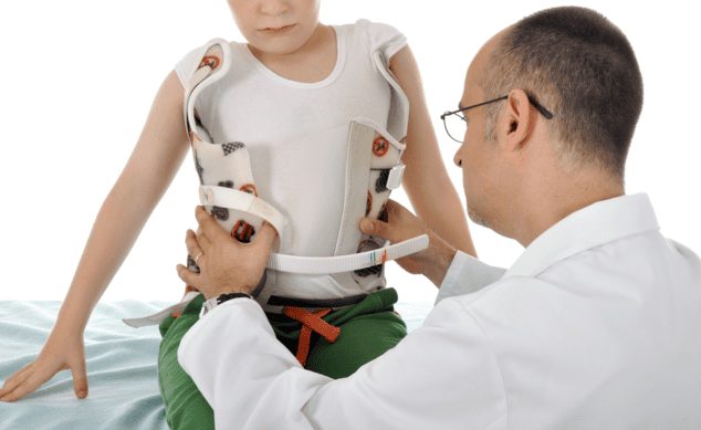 Un médico ajuste cuidadosamente un corsé a un niño diagnosticado con escoliosis, un paso importante en su tratamiento